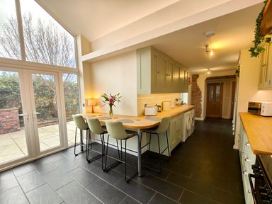 A kitchen with high chairs at a wooden counter and large glass doors at Grove House Egremont