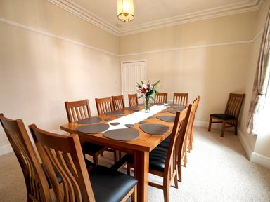 A dining room with a wooden table set with placemats and a vase of flowers in the center at Grove House in Egremont