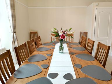 A dining room with a wooden table and matching chairs with gray placemats and a flower vase at Grove House in Egremont