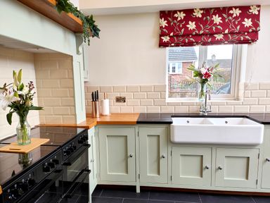 A kitchen with light green cabinets a white double sink a black stove and flowers on the counter at Grove House in Egremont