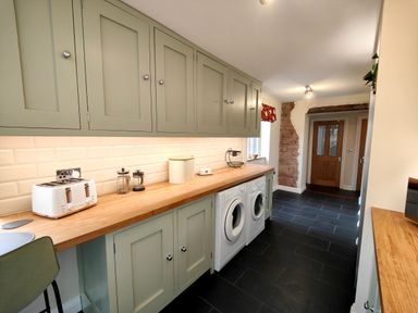 A utility room with green cabinets wooden countertop washing machine dryer and toaster at Grove House in Egremont