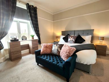 A bedroom with a bed headboard bedside tables lamps a desk with drawers and a blue sofa with pillows at Grove House in Egremont