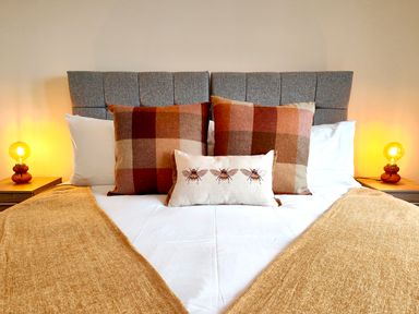 A bed with a gray headboard two large checkered pillows a smaller pillow with bee designs two bedside tables with lamps at Grove House in Egremont