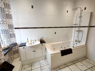 A bathroom with a bathtub and shower, a sink with a cabinet, tiled walls and floor at Grove House in Egremont