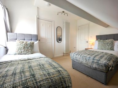 A bedroom with two single beds with grey headboards and patterned blankets at Grove House in Egremont