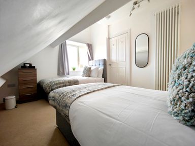 A bedroom with two single beds a window a wooden chest of drawers and a wall mirror at Grove House in Egremont