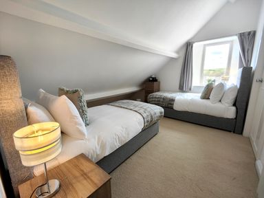 A bedroom with two single beds a bedside table with a lamp a window and a wooden chest of drawers at Grove House in Egremont