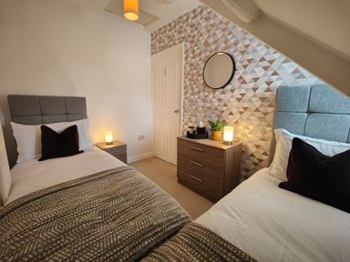 A bedroom with two single beds bedside tables a chest of drawers and a round mirror at Grove House in Egremont