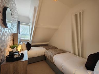 A bedroom with two single beds a bedside table with decor a window and a decorative mirror at Grove House in Egremont