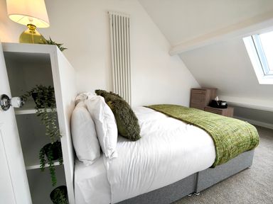 A bedroom with a bed covered in white sheets and green blankets under a skylight window at Grove House Egremont