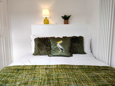 A bed with white sheets green pillows and a green throw blanket with a lamp and plant on the headboard at Grove House in Egremont