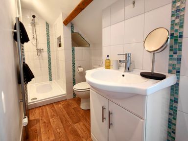 A bathroom with a shower area, toilet, sink with cabinet, mirror, and wooden floor at Grove House in Egremont