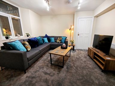 A living room with a gray sectional sofa with blue pillows a wooden coffee table and a TV on a wooden stand at Grove House in Egremont