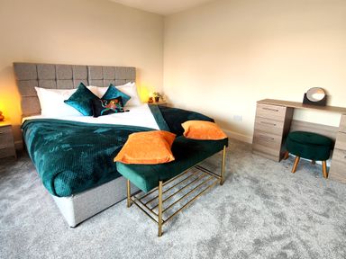 A bedroom with a bed a bench with orange pillows a dressing table and a stool at Grove House in Egremont