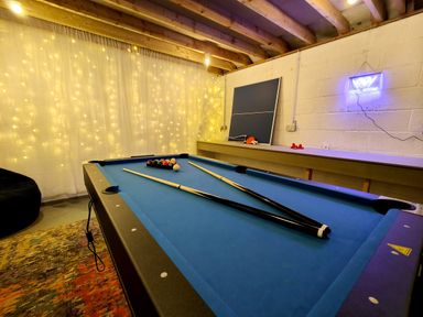 A pool table with pool cues and balls a ping pong table and a neon pool room sign in a game room at Grove House in Egremont
