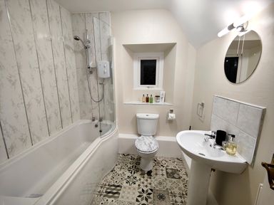 A bathroom with a bathtub shower, toilet, sink, and patterned floor at Grove House in Egremont