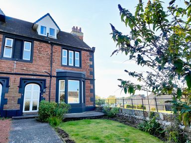 A garden with grass and plants next to a brick house with multiple windows at Grove House in Egremont