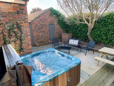 An outdoor patio area with a hot tub black metal chairs a black metal table a wooden picnic table a tree and a brick shed at Grove House in Egremont