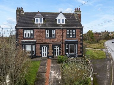 A two-story brick semi detached house with front gardens and a driveway by a curved road at Grove House in Egremont