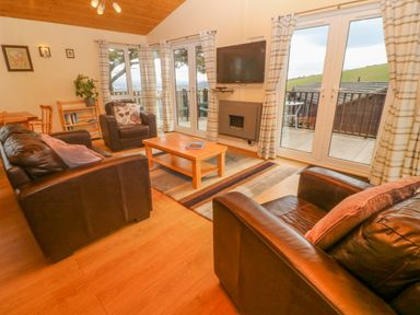 A living room with leather sofas a coffee table a wall-mounted TV and glass doors opening to a balcony at Lodge 23 in Torpoint