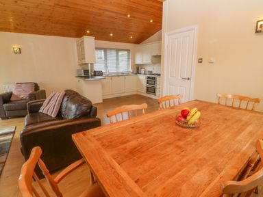 A kitchen with white cabinets next to a dining area with a wooden table and chairs and a living area with brown leather sofas at Lodge 23 in Torpoint