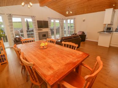 A dining area with a wooden table and chairs next to a living room with leather sofas and a wall-mounted TV at Lodge 23 in Torpoint