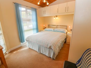 A bedroom with a double bed with checked bedding and blue curtains at Lodge 23 in Torpoint