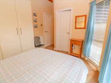 A bedroom with a bed covered in a plaid bedspread a white wardrobe a wooden nightstand and a window with blue curtains at Lodge 23 Torpoint