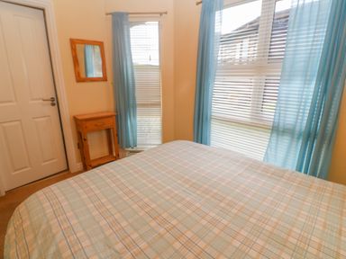 A bedroom with a bed covered by a plaid bedspread a wooden nightstand and two windows with blue curtains at Lodge 23 Torpoint