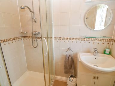 A bathroom with a shower enclosure a sink with cabinet a round mirror a towel ring with towel and a soap dispenser at Lodge 23 in Torpoint