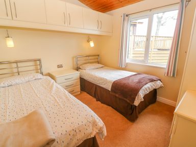 A bedroom with two single beds a nightstand between them wall cabinets a window and curtains at Lodge 23 in Torpoint