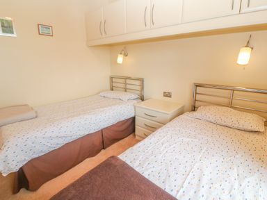 A bedroom with two single beds a nightstand and wall-mounted lamps at Lodge 23 in Torpoint