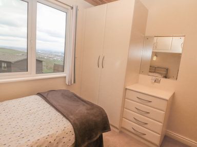 A bedroom with a bed next to a window a tall wardrobe and a chest of drawers with a mirror at Lodge 23 in Torpoint