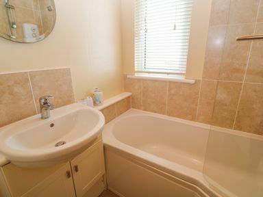 A small bathroom with a sink and cabinet next to a bathtub with tiled walls and a window with blinds at Lodge 23 in Torpoint