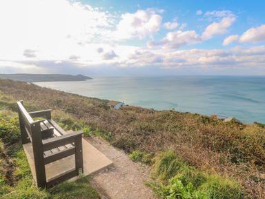 A bench on a path overlooking the ocean with bushes and a small house on a hillside at Lodge 23 in Torpoint