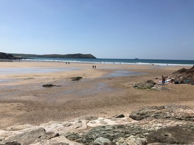 A sandy beach with scattered rocks people walking and a small hill in the background at Lowenda in Polzeath