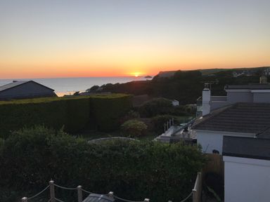 A sunset over the ocean with houses and gardens in the foreground at Lowenda in Polzeath