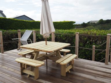 An outdoor wooden deck with a picnic table and benches and a folded umbrella at Lowenda in Polzeath
