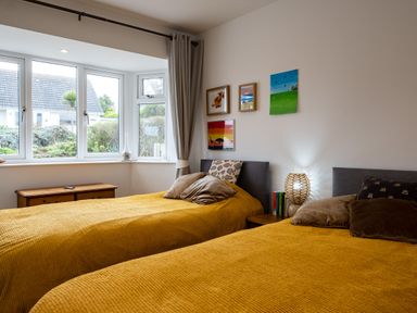 A bedroom with two single beds with yellow bedspreads and a window overlooking a garden at Lowenda in Polzeath