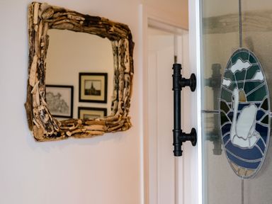 A door with a black handle and stained glass decoration next to a wall mirror with a wooden frame at Lowenda in Polzeath