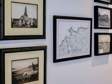 A wall with framed black and white photographs and a map at Lowenda in Polzeath