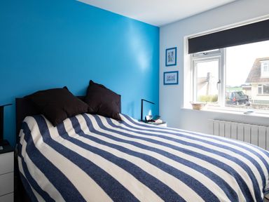A bedroom with a blue and white striped blanket on the bed and a blue accent wall at Lowenda in Polzeath