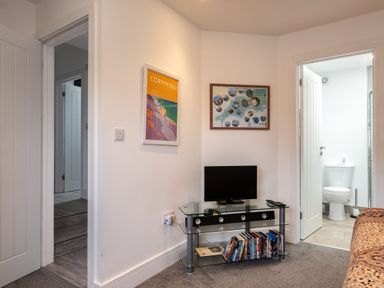 A small living area with a TV on a glass stand and a bathroom visible through an open door at Lowenda Polzeath