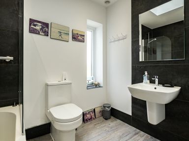 A bathroom with a toilet a sink a mirror a bathtub and framed photos on the wall at Lowenda Polzeath