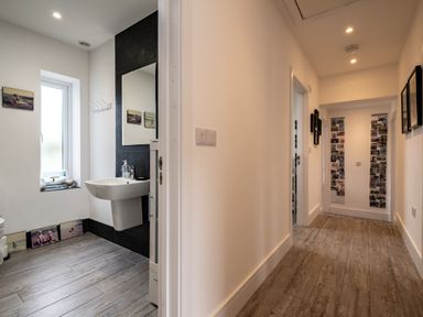 A hallway with wooden floor and framed pictures leading to a room with a sink and window at Lowenda in Polzeath