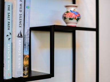 A black metal shelf with three books and a small floral vase on a wall at Lowenda in Polzeath