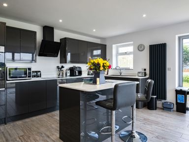 A kitchen with black cabinets an island with chairs and flowers on the countertop at Lowenda in Polzeath