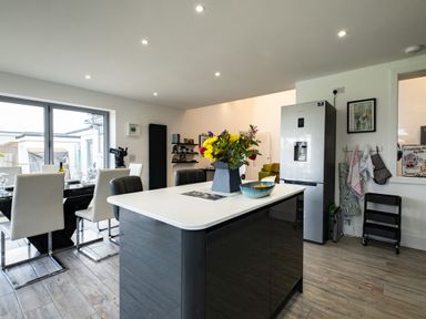 A kitchen and dining area with a kitchen island and flowers on it and a dining table with chairs at Lowenda in Polzeath