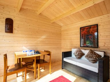 A wooden room with a small table and two chairs a chess set on the table a wicker sofa with cushions and a framed picture on the wall at Lowenda in Polzeath