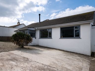 The exterior of a single-story house with white walls gray windows a concrete driveway and a bush in front at Lowenda in Polzeath